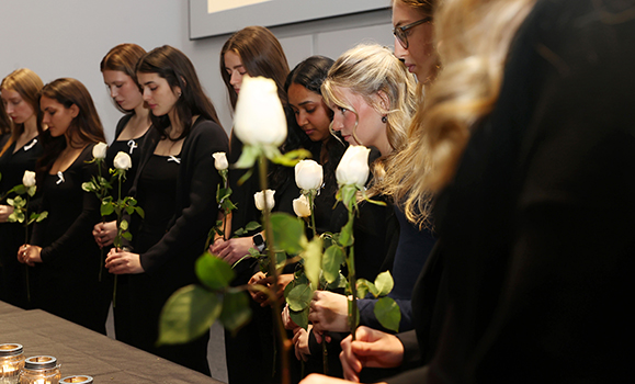 women wearing black and holding white roses stand in a moment of remembrance