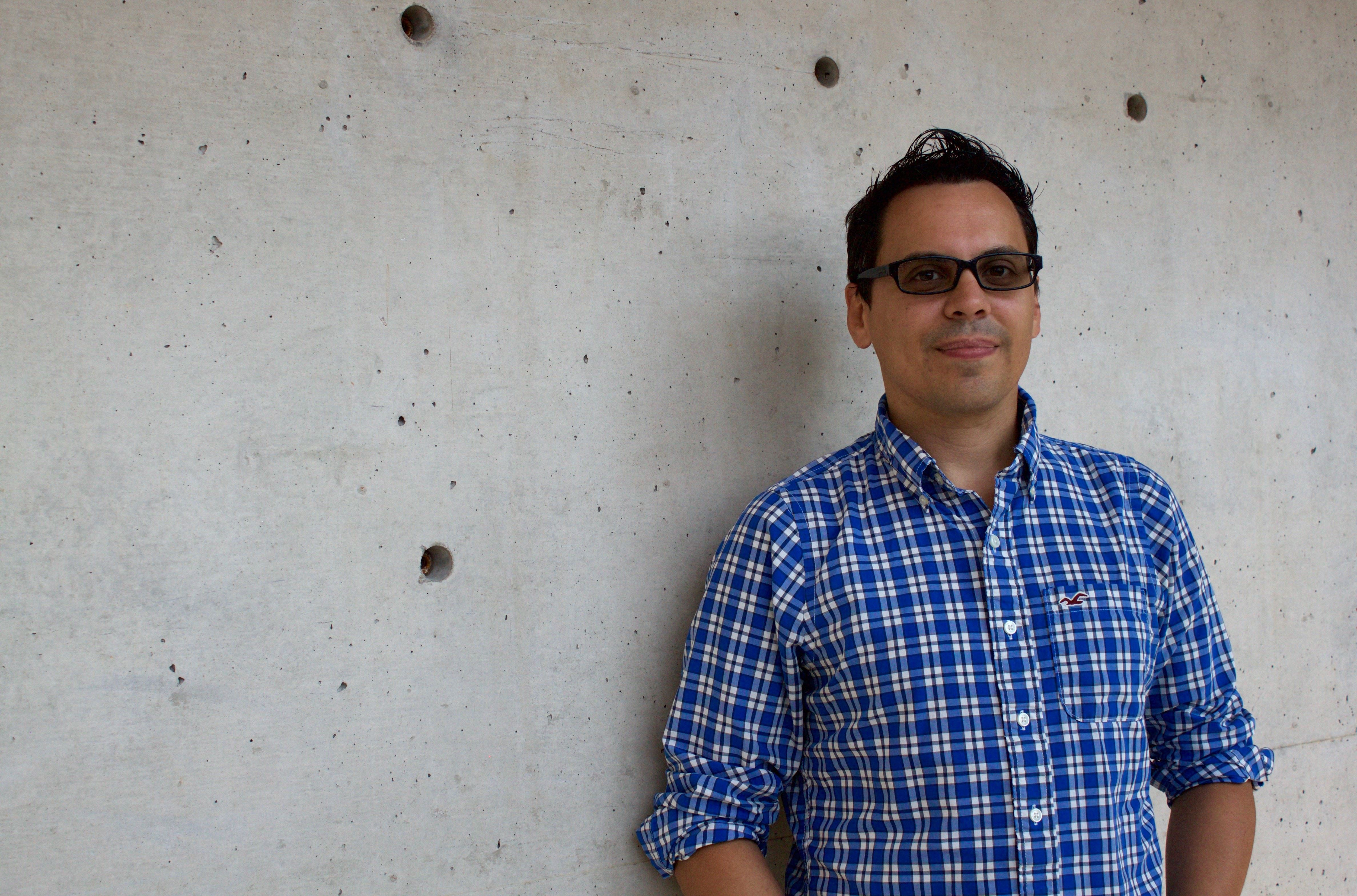 Andrew looks at the camera. He has a medum-light skin tone, short black hair, and glasses with dark lenses.