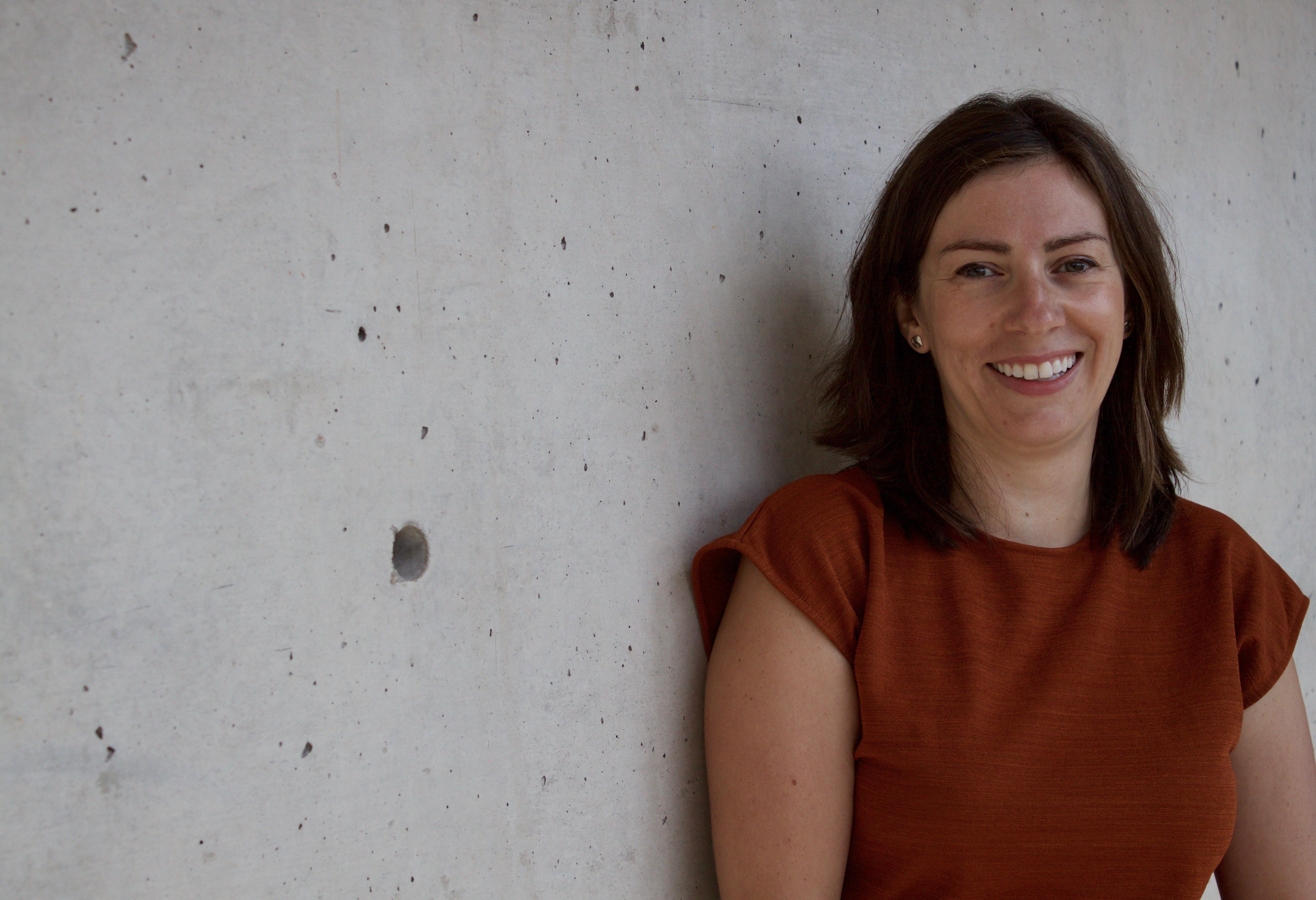 Melanie smiles at the camera. She has a light skin tone and shoulder-length brown hair.