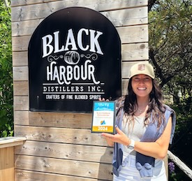 Jaime poses with an award plaque in front of a Black Harbour sign.
