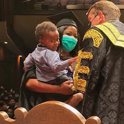 Rebecca and her son on stage accepting her degree at convocation. Rebecca is grinning under her mask, talking to a 鶹ý official, and Ethan is smiling at the person taking the photo. 