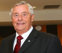 Rowe, a white man with grey hair wearing a suit and tie, smiles at the camera. 