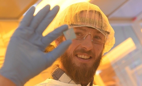 Dr. Sam March, Co-founder of Rayleigh, is wearing protective gear while holding a solar cell close to the camera.