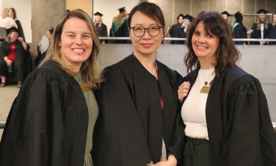 Three staff members dress in black gowns smile at the camera.