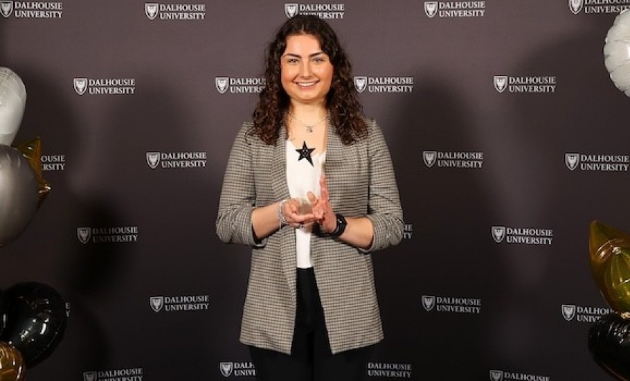 Sophika Dmytryshyn dressed in businesswear, smiles in front of a Dalhousie photo backdrop.
