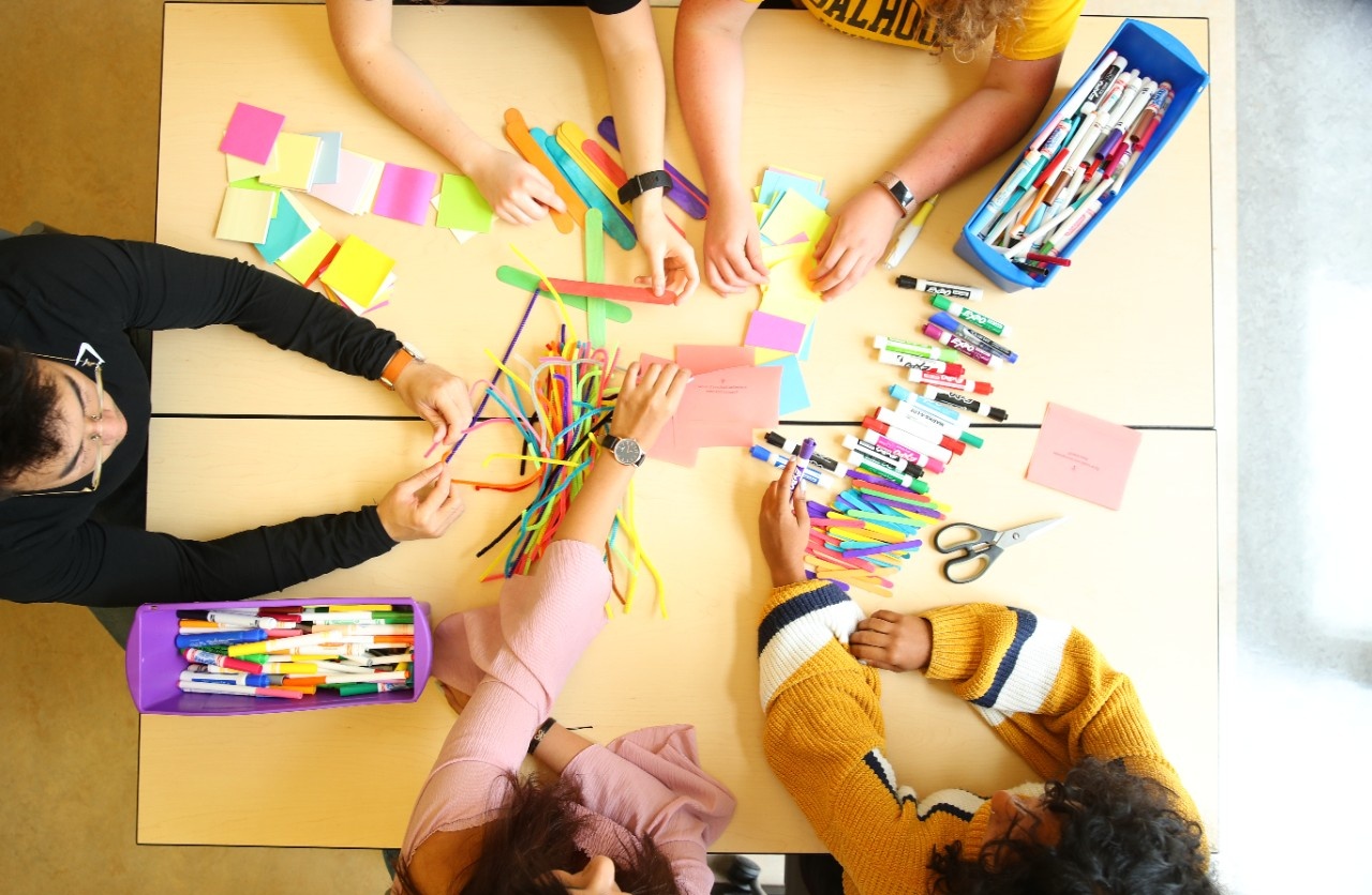 Overhead image of four students participating in a learning exercise with colourful sticky notes and markers.