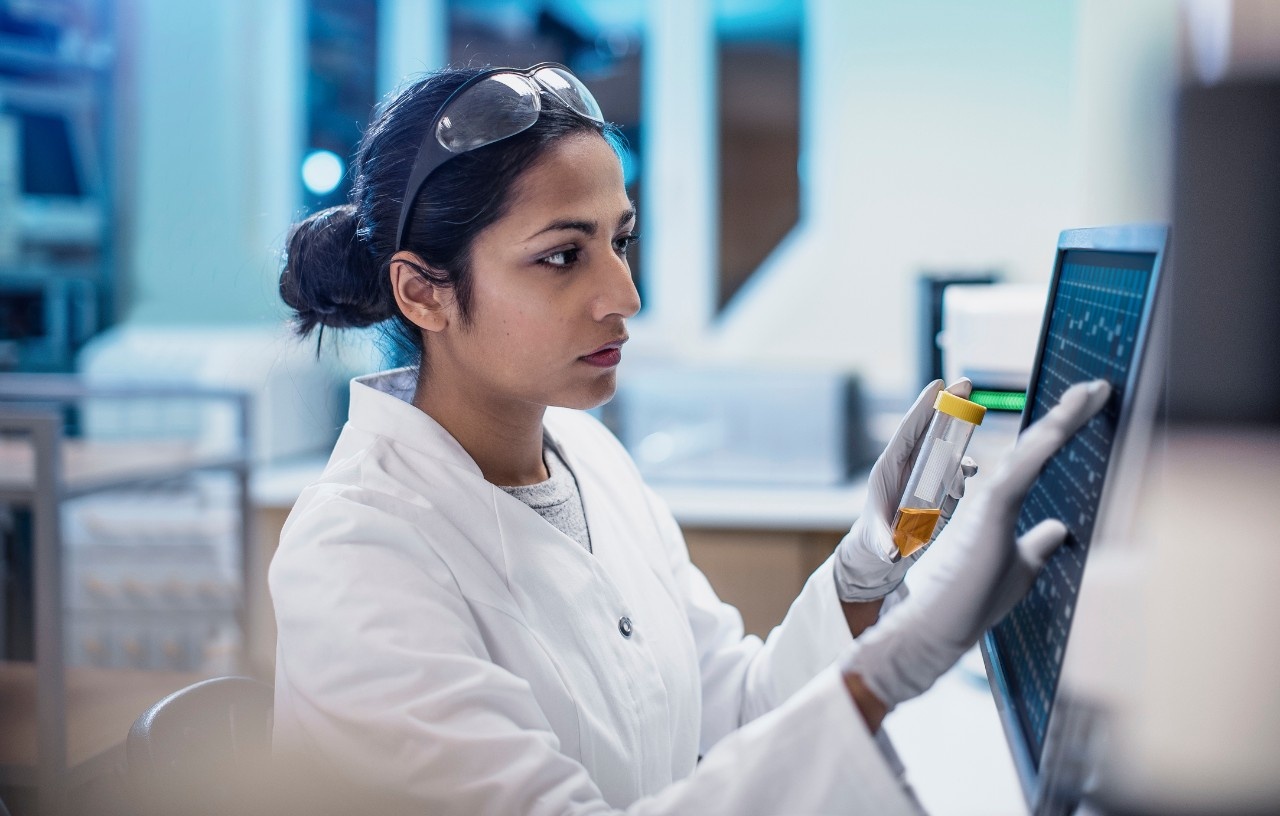 Woman in laboratory wearing white jacket inputs data into a computer.