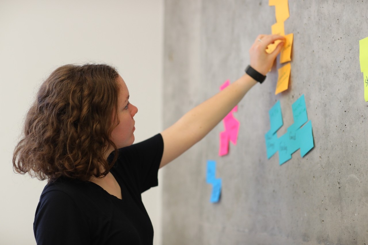 Young woman removes a colourful sticky note from a wall during a learning exercise.