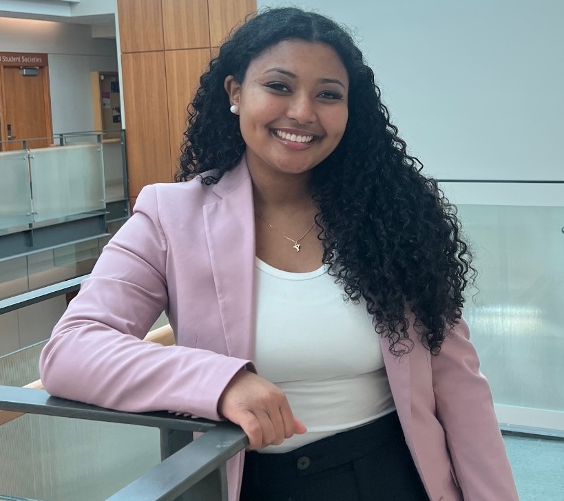 Yasmine leans on a balconey railing, smiling at the camera.