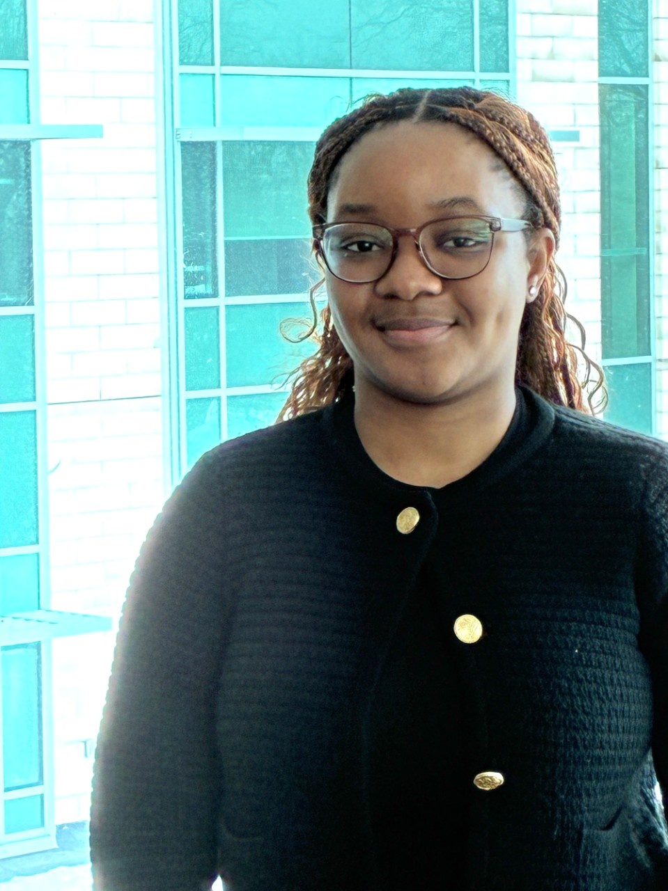 Rose stands in front of a window in the Rowe Building, wearing a black sweater.