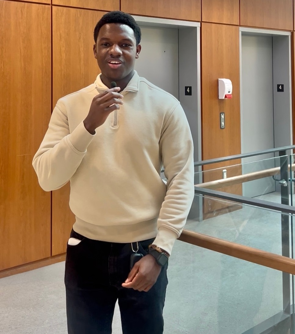 Vincent speaks into a microphone, wearing a white zippered sweater.