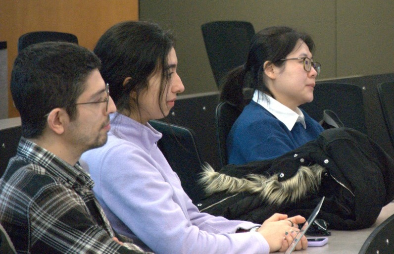 Three student audience members watch intently.