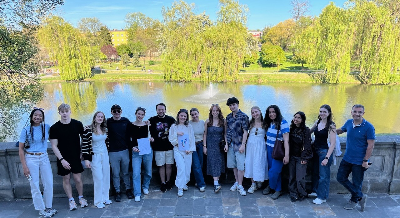 A group of students pose in front of a lake with trees in the background.