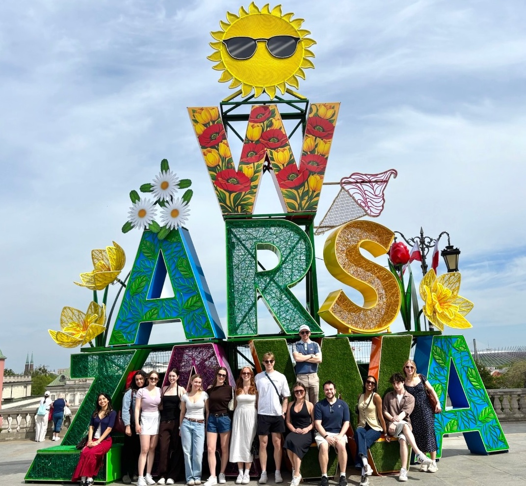 A group of students pose in front of a sign that says Warszawa in brightly coloured letters.