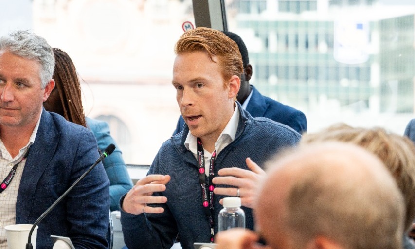 Michael gestures while emphatically while speaking, seated in a room with a wide window behind him.