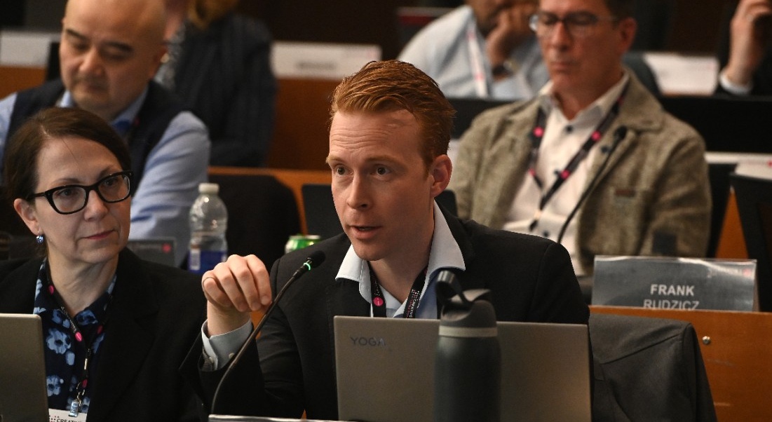 Michael speaks into a microphone seated at a desk with a laptop in front of him.