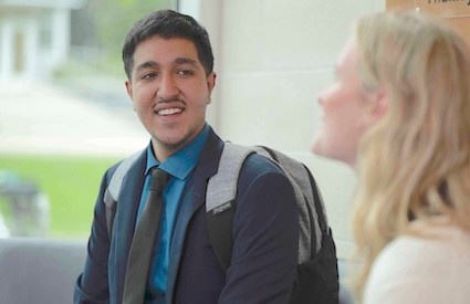Pratik, wearing a suit, smiles as he listens to someone out of focus in the foreground.