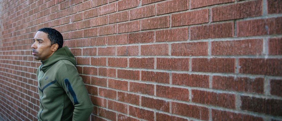 Rodney Small, wearing a green sweatshirt, leans against a brick wall.