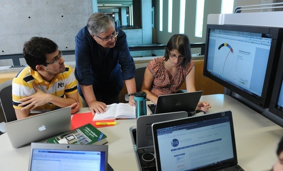 Students and a professor reviewing data on laptops and large monitors. Students and a professor reviewing data on laptops and large monitors.