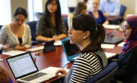 Students sit in a boardroom with laptops, focusing on a speaker off-screen. Students sit in a boardroom with laptops, focusing on a speaker off-screen.
