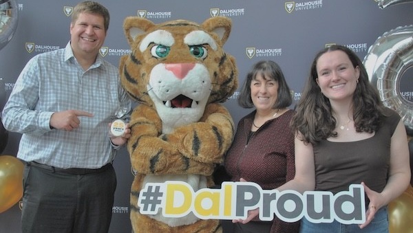 A student, two professors, and the Dal tiger mascot stand with a sign that says #DalProud.