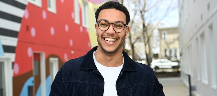 Mohammed Hamedelniel stands outside, smiling, with a brightly coloured mural behind him.