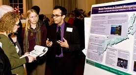 Two graduate students present a poster to someone with a clipboard