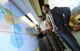 Students standing at a data wall, pointing at diagrams.