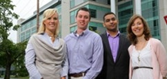 4 MBA students dressed professionally standing  in front of the Rowe Building, smiling at the camera.