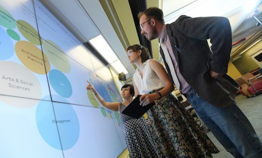 Three MI students examine the data visualization wall in the Killam Library.