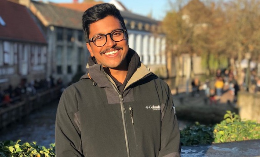 Chris Fernandes stands outdoors in a jacket and glasses with buildings along a canal in the background.