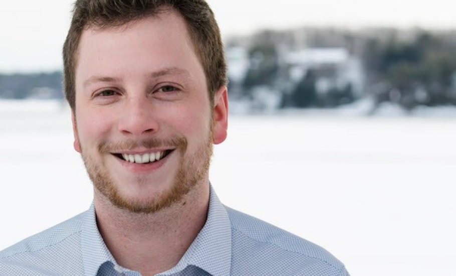 A close up of Ben John's face . He is outdoors with water in the background.