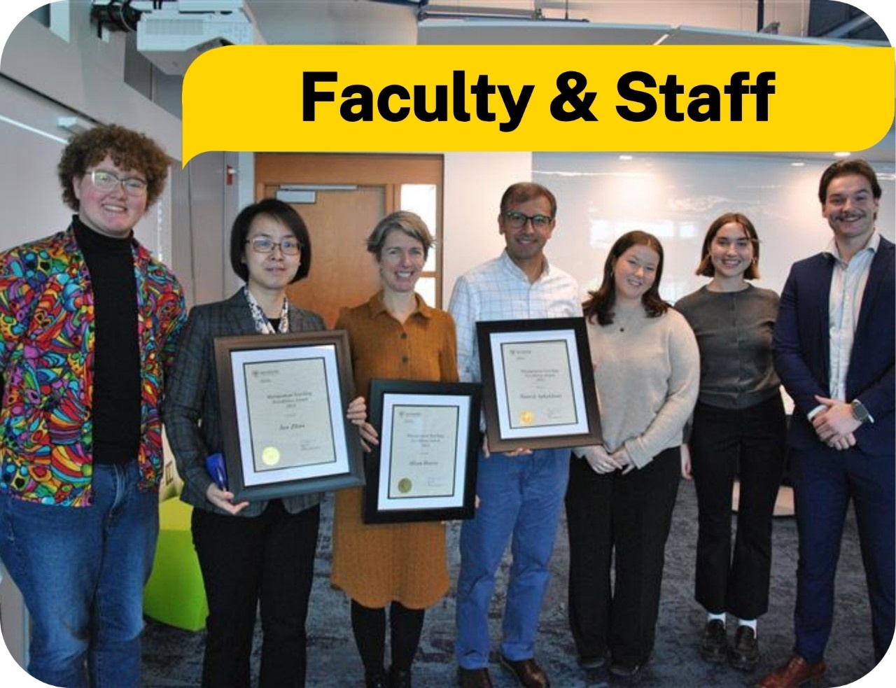 A group of professors holding awards certificates in a classroom. Text: faculty and staff.