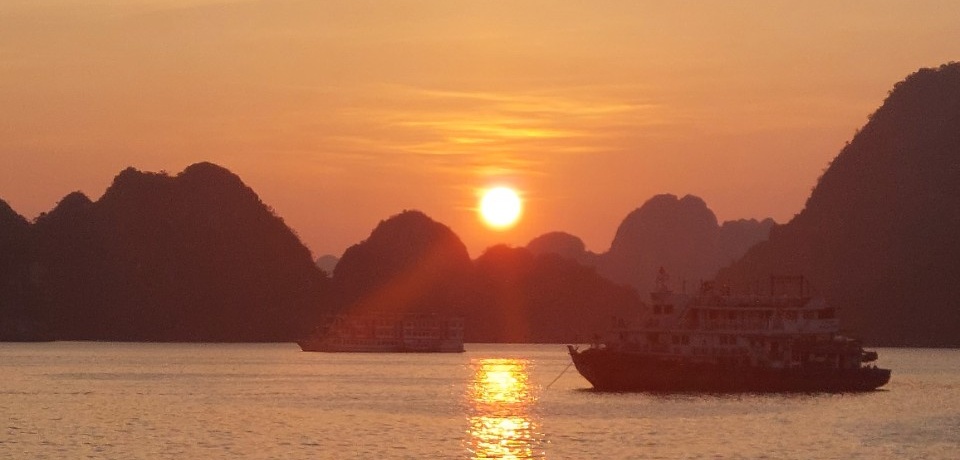 A boat on the water at sunset with mountains in the background.