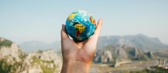 A hand holds up a small globe against a backdrop of mountains.