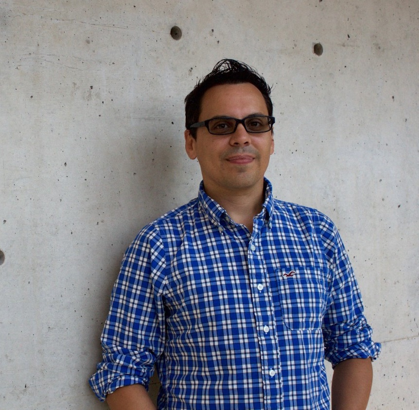 Andrew is smiling. He has a medium-light skin tone and short black hair, and is wearing dark-tinted glasses and a blue-and-white checkered shirt.