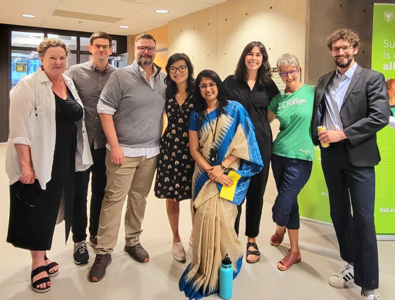 A group of eight faculty and staff members pose together in front of the College of Sustainability main doors, smiling.