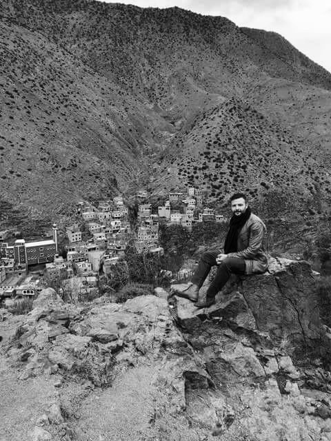 Andrew poses for a picture on a ridge in the Atlas Mountains in Morocco, with a town far below in the background.