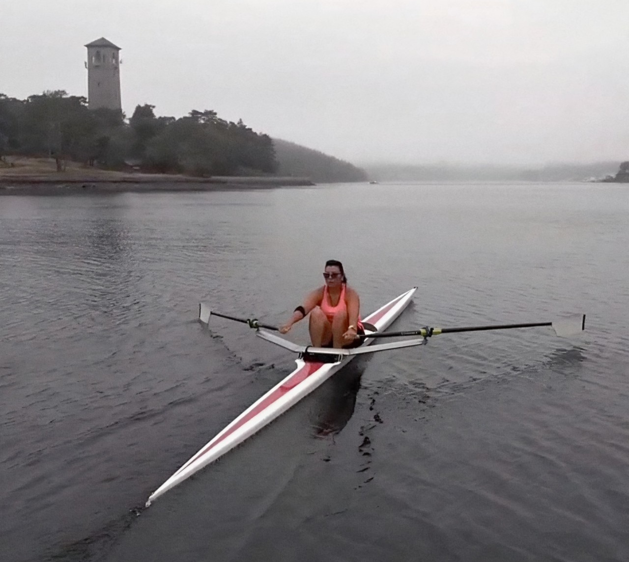 On a foggy day, San rows a small, thin boat across the empty north-west arm of Halifax Harbour. Trees and the Dingle Tower are visible on the shoreline nearby. On a foggy day, San rows a small, thin boat across the empty north-west arm of Halifax Harbour. Trees and the Dingle Tower are visible on the shoreline nearby.