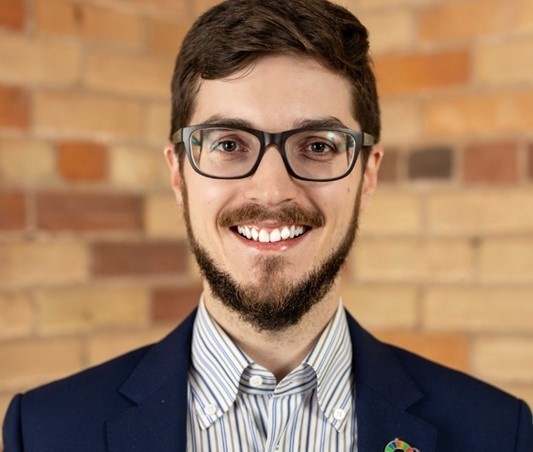 Lars smiles at the camera. He has a light skin tone, glasses, short dark hair and a neatly-trimmed beard.