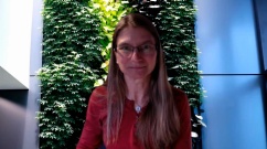 Kaarin Tae sits in front of a green wall covered in plants.