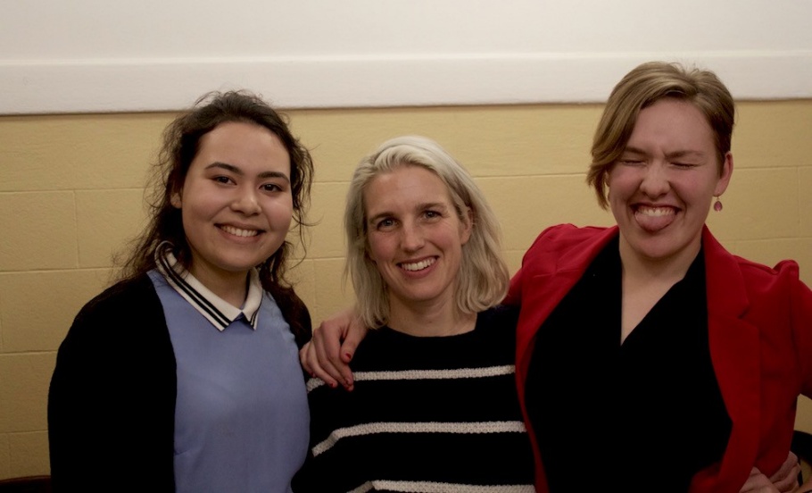 Three people stand together closely, arms over each other's shoulders, and smile for the camera.