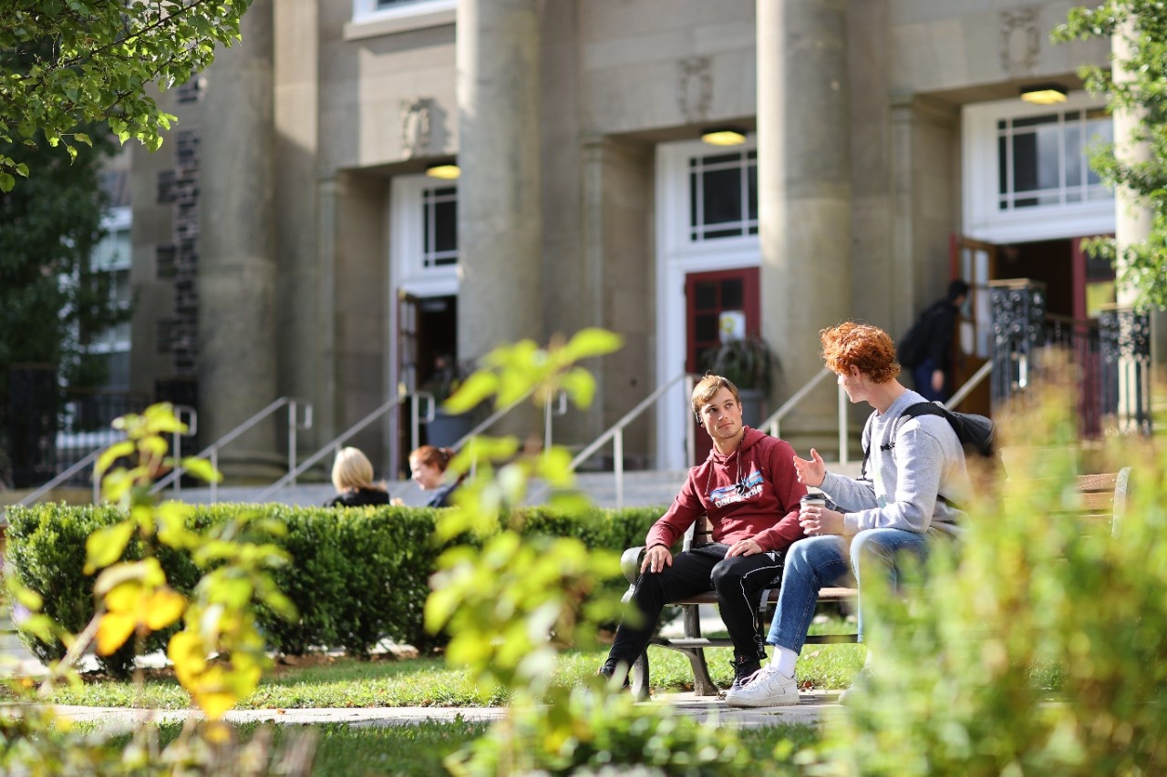 Students sitting on a bench in front of the Henry Hicks Building.