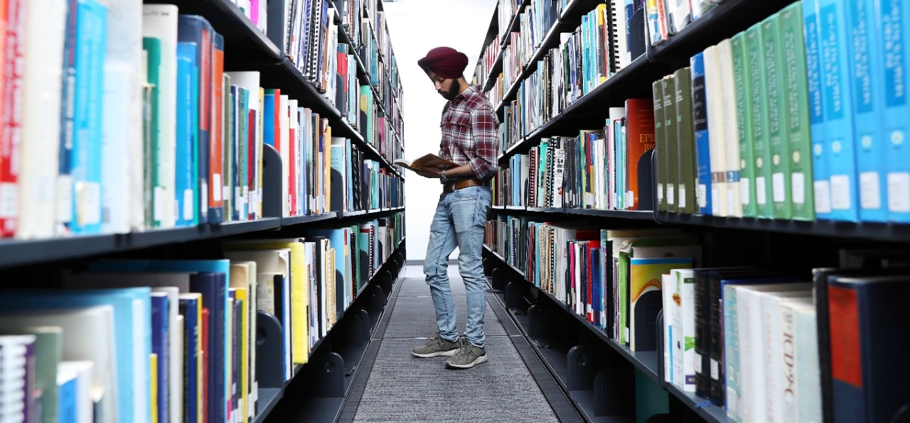 a female student looks through a large book while standing in the book stacks at the Killam Library