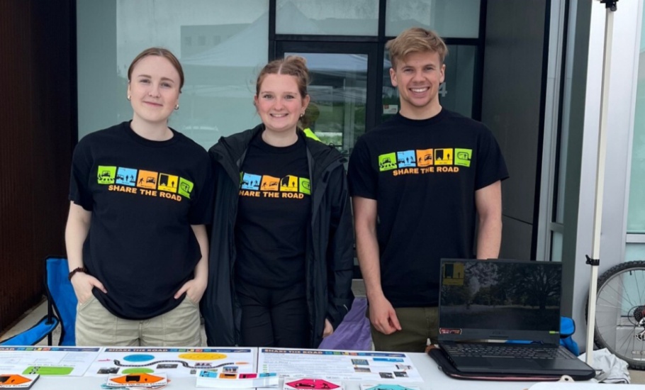 A group of students posing in front of the share the road booth at the 2024 heartland tour