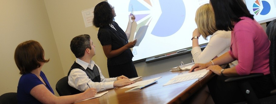 A student makes a presentation to 4 other students sitting around a table.