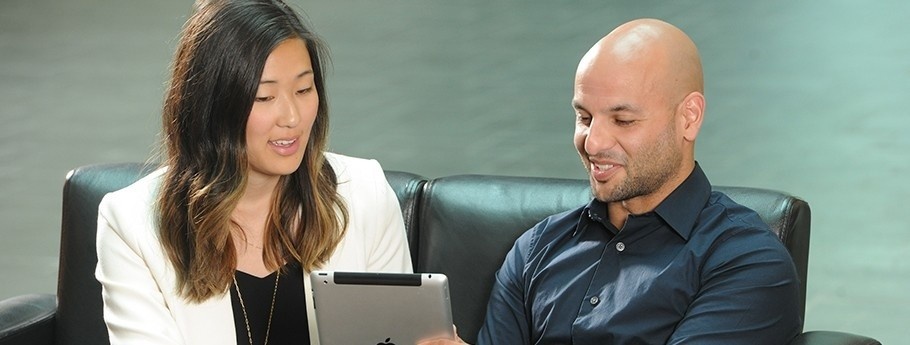 Two students sit on a couch, consulting a tablet.